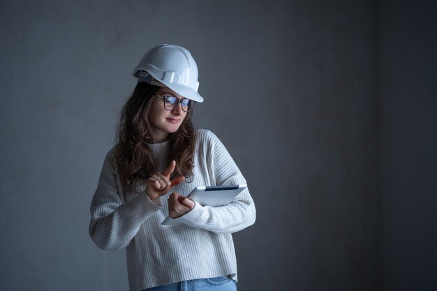 Молодая женщина-архитектор использует планшет внутри здания с бетонной стеной во время строительства