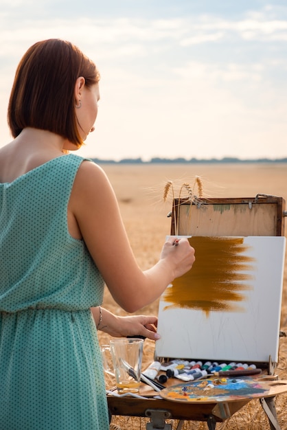 Photo young female artist drawing a picture in the field of ripe rye