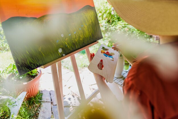 Foto giovane artista che lavora alla sua tela d'arte dipingendo all'aperto nel suo concetto di terapia artistica del giardino