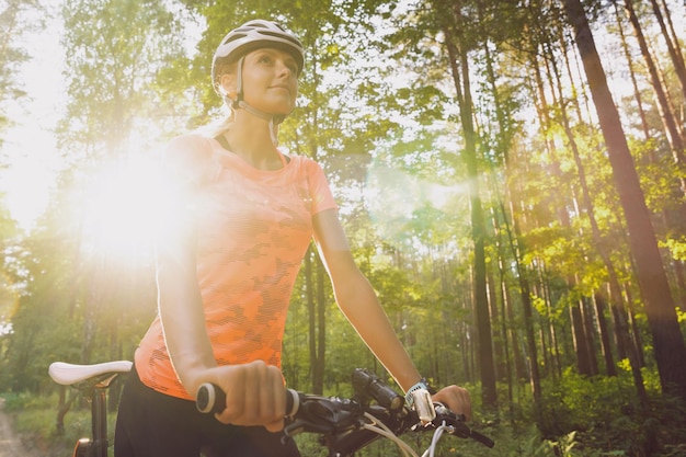 屋外でのトレーニング中にヘルメットとオレンジ色のTシャツを着た若い女性アスリートサイクリスト