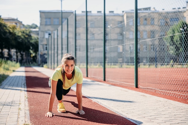 Young female athlete with dark hair starting to run on red track.