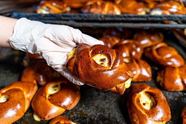 Young female baker wearing oven mitts and holding a tray of freshly baked buns in a bakery