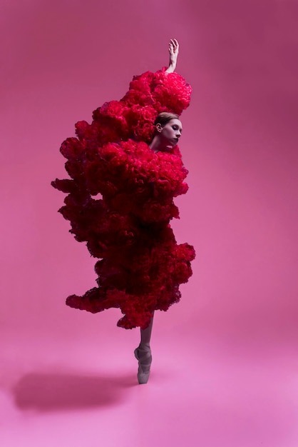 young female ballerina in a photo studio in a cape dress made of rose flowers shows ballet movements