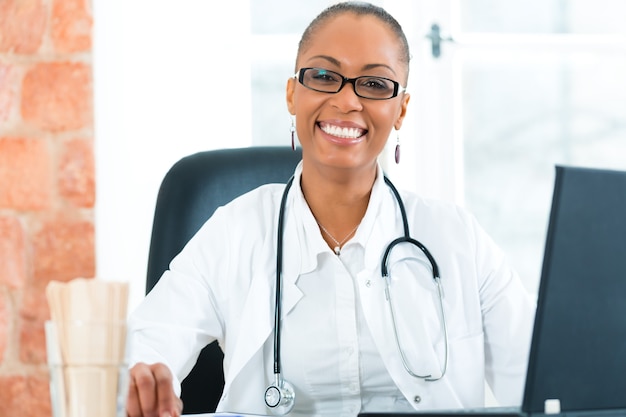 Young female black doctor sitting at a window in clinic, she has a stethoscope