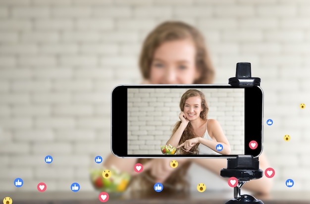 Young female blogger and vlogger and online influencer live streaming a cooking show on social media using a smartphone