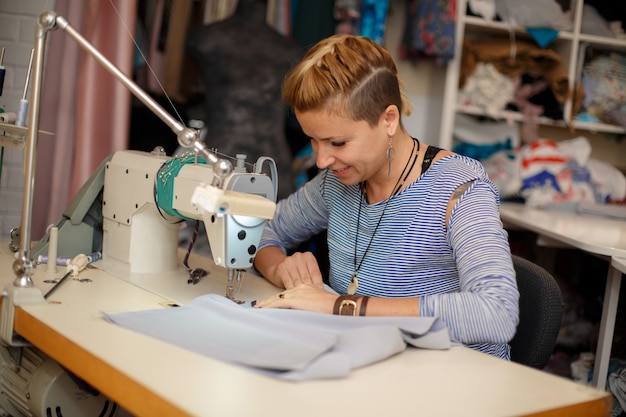 Young female blonde dressmaker works on sewing machine. dress manufacturing industry