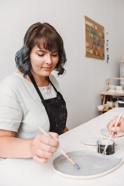 Young female ceramist working by hands in pottery studio.