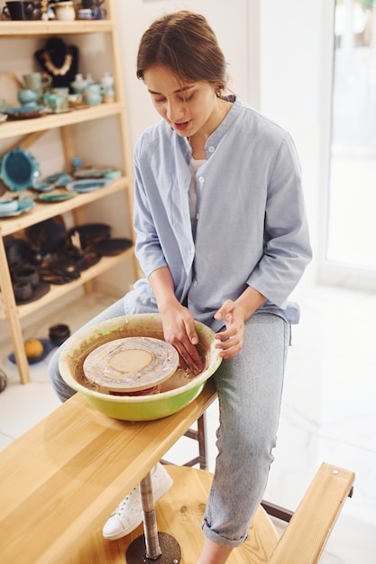 Молодая женщина-керамист, работающая с использованием гончарного круга в помещении и изготавливающая изделия из глины ручной работы