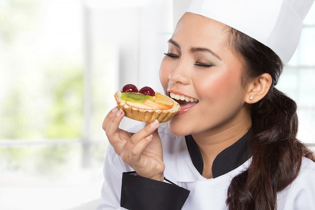 Young female chef eats small cake