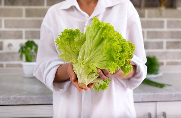 Young female chef shows a beam of lettuce and a bunch of spinach