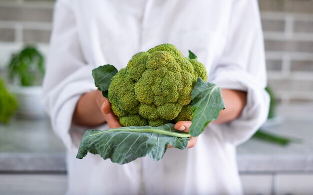 Young female chef shows the camera a head of broccoli