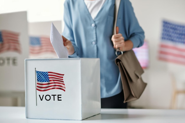 Young female citizen of United States of America putting paper into ballot box