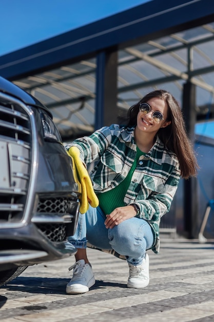 A young female cleaning and polishing her car with yellow\
microfiber cloth concept of car taking care