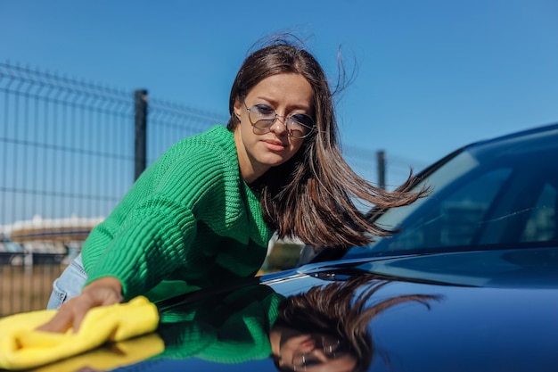 Una giovane donna che pulisce e lucida la sua auto con un panno in microfibra giallo concetto di cura dell'auto