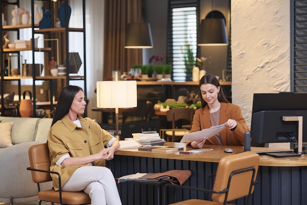 Young female client sitting in front of creative designer of interior