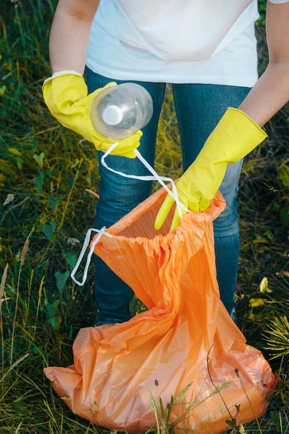 Young female collecting trash and putting in plastic garbage bag - environmental pollution concept