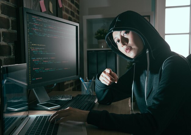 young female computer programmer as hacker doing illegal working online and looking at camera pointing showing threat concept.