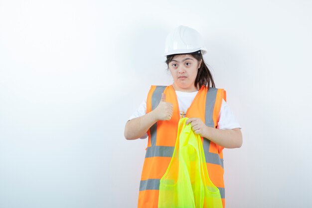 Young female construction worker in hardhat wearing vest over white wall. 