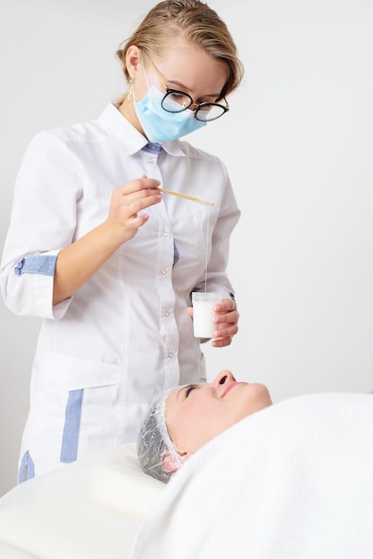 Young female cosmetologist applies cosmetic product on the face of female patient Spa cosmetic pro