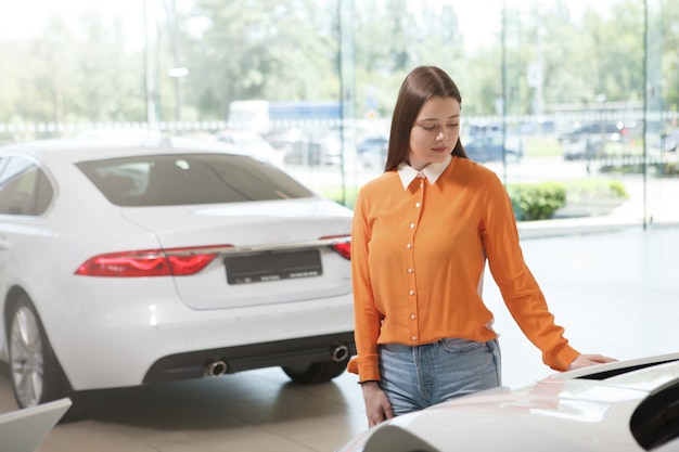 Young female customer examining cars for sale at dealership salon, copy space