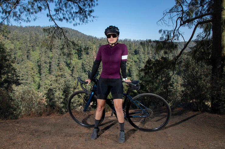 Young female cyclist posing with her bike at a viewpoint with a wooded landscape in the background