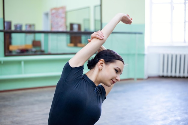 Young female dancer going physical stretching before lesson of choreography