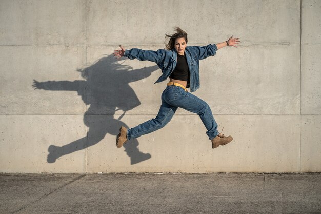 写真 灰色の背景と反射した影でジャンプする若い女性ダンサー。横向き写真