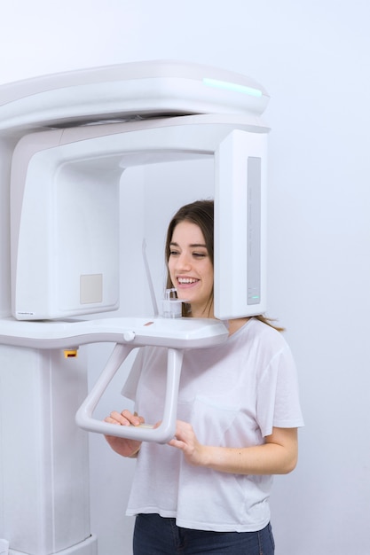 Young female dental patient standing in digital cephalometric panorama x-ray machine