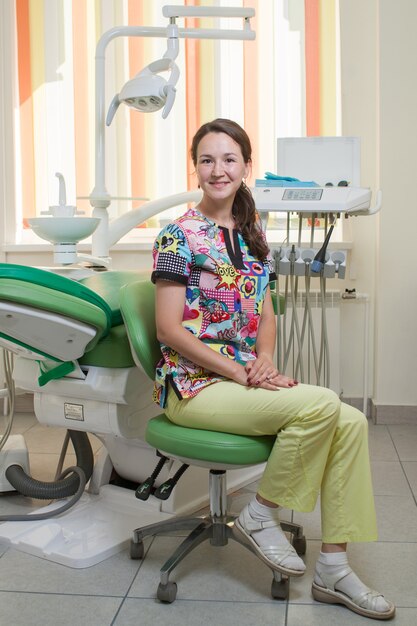 Photo young female dentist on dental chair next to dental dashboard