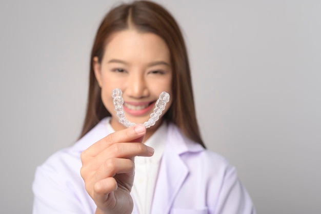 Молодая женщина-стоматолог держит брекеты invisalign на белом фоне студии