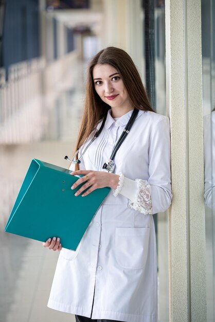 Young female dentist in a special uniform stands in the corridor smiling with her ideal teeth