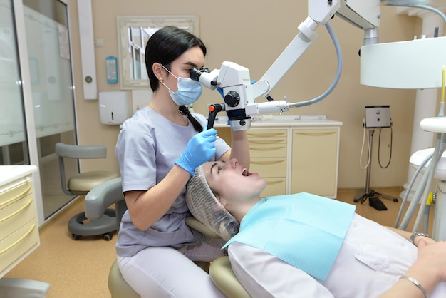 La giovane dentista femminile tratta i canali radicolari usando un microscopio in una clinica odontoiatrica