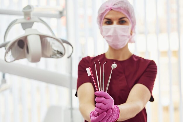 Young female dentist in uniform standing in stomatology office holding brush and tools