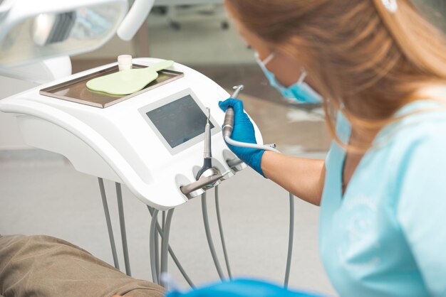 Young female dentist wearing uniform is in the work process with dentistry tools near chair