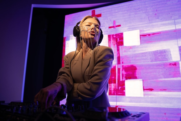 Young female DJ in a nightclub at the console the girl is wearing a white suit and jewelry on her face