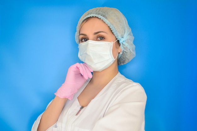 青色の背景に若い女性医師。ヘルスケアおよび医学の概念。白衣の医師、ピンクの手袋、フェイスマスク。パンデミックのコンセプト