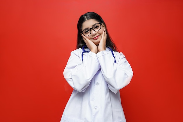 young female doctor front view hands on cheeks on red background indian pakistani model