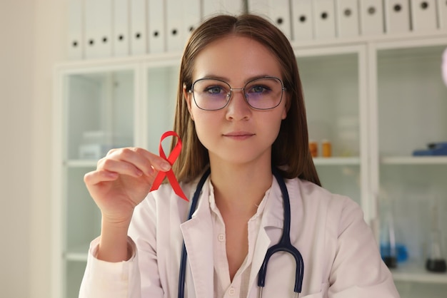 Young female doctor in glasses holding red ribbon as symbol of aids disease international world