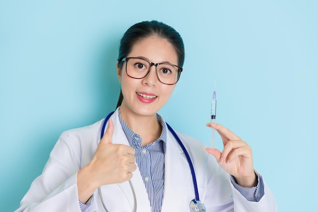 young female doctor holding injection and showing a thumbs up with friendly smile happily.