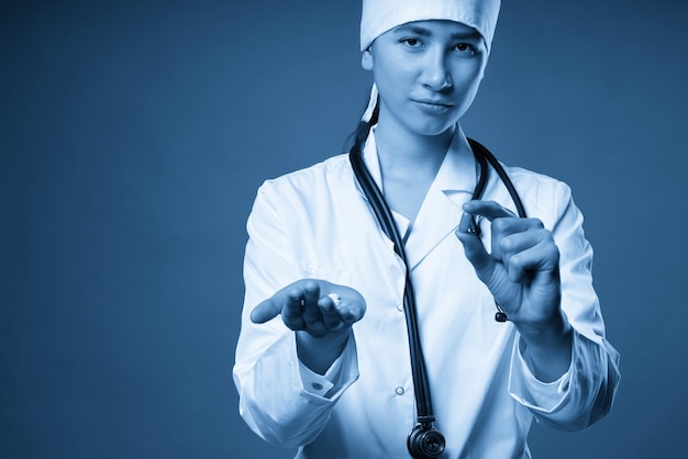 Young female doctor holding a pill looking at it and giving it as a treatment to the patient