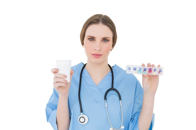 Young female doctor holding a plastic cup and medicine looking into the camera