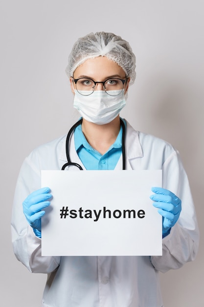 젊은 여성 의사가 해시 태그 #stayhome으로 종이를 들고있다