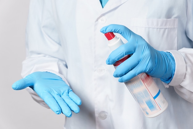 Young female doctor makes an additional disinfection of the gloves with a alcohol spray