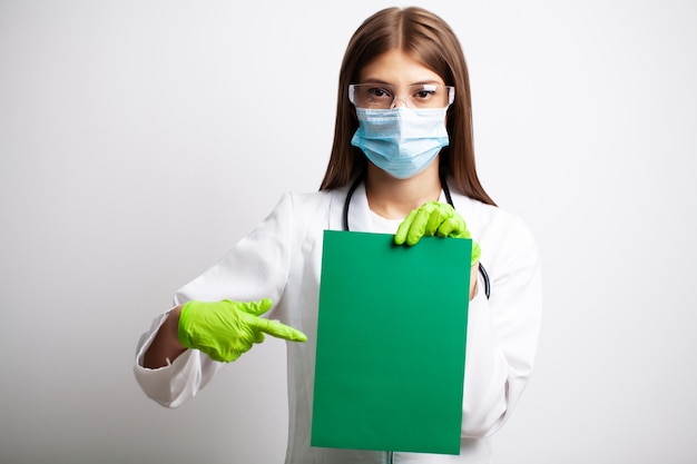 Young female doctor in a mask holds a blank sheet of paper