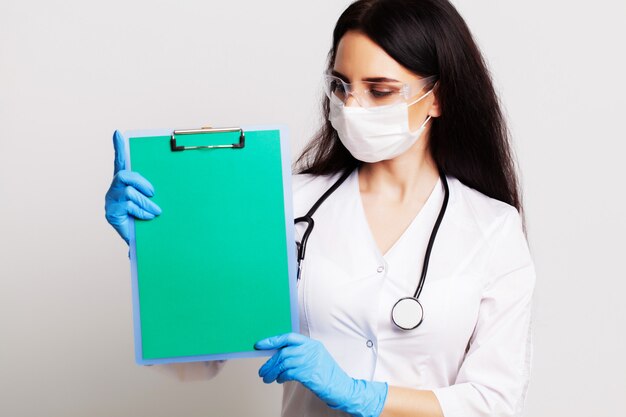 Young female doctor in a mask holds a blank sheet of paper