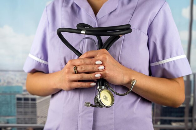 Young female doctor in a medical gown with short sleeves holds\
a stethoscope hanging around her neck medicine female doctor close\
up photo