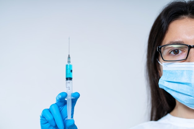 Молодая женщина-врач в медицинской маске и перчатках держит шприц с вакциной от коронавируса и чипом вакцины внутри. Теория заговоров. Чипирование людей.