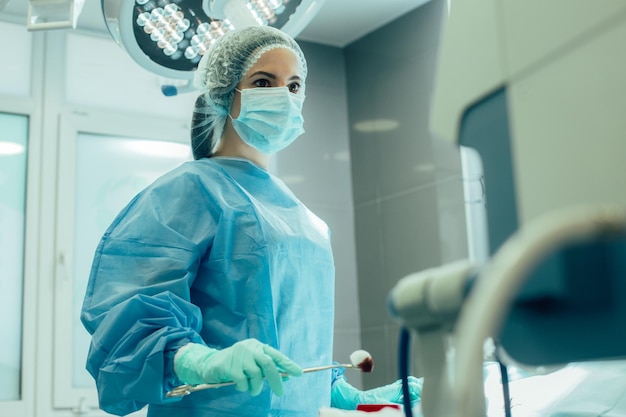 Young female doctor in medical uniform holding a bloody piece of cotton wool with forceps and looking at the monitor