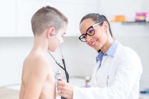 Young female doctor pediatrician examines playfully boy patient.