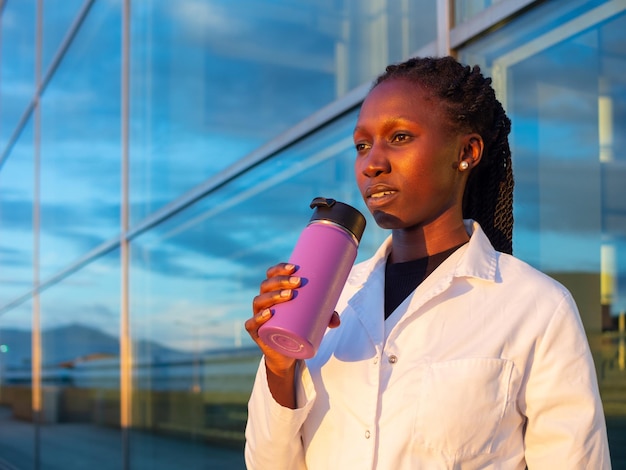 young female doctor or scientist drinking from a coffee thermo during her break